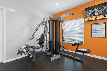A home gym with a weight machine, a bench, and a television screen showing a basketball game.